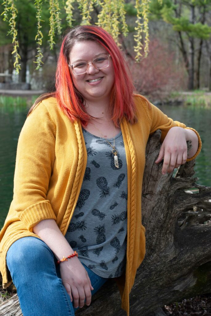 Cindy Marceau, doula aux cheveux oranges, assise à l'extérieure sur un tronc d'arbre.