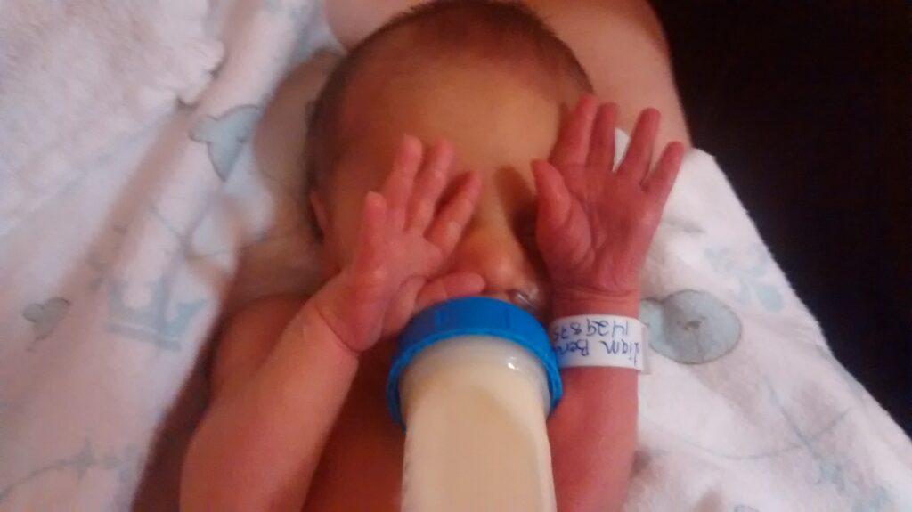 Bébé qui boit son lait en cachant ses yeux avec ses mains, paumes vers le haut