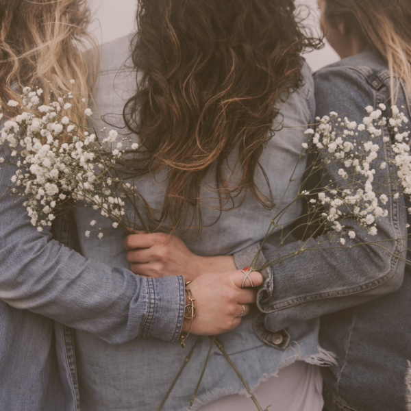 Trois femmes de dos, se tenant par la taille et tenant un bouquet de fleurs blanches minimalistes à la main
